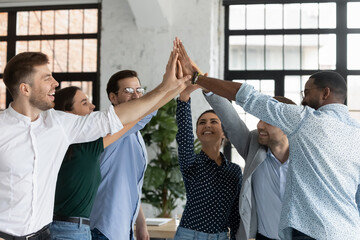 Overjoyed successful young diverse employees giving high five at corporate meeting, celebrating...