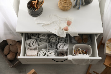 Modern open chest of drawers with baby clothes and accessories in room, above view