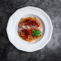 plate with a portion of delicious italian spaghetti with sauce bolognese with fresh basil leaves and grated parmesan cheese on the cement background, top view, flatlay, square photo