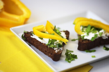 Slice of black bread with cheese cream, yellow pepper and herbs close-up