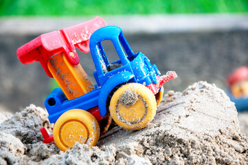 Children s toy car, colorful plastic lorry on sand. Close-up. Selective focus. Copy space.