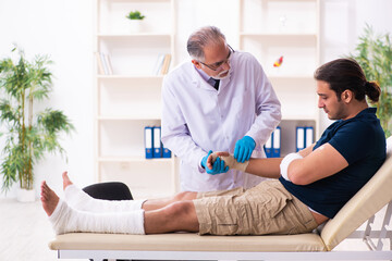 Fototapeta premium Young injured man visiting old doctor traumatologist