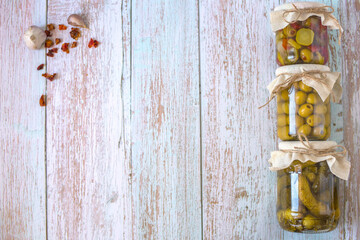 Canned cucumbers, fermented vegetables salad and pickled olives on white wooden background. Homemade conservation, top view