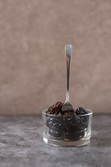 Pickled plums in glass bowl with fork on gray background, vertical orientation