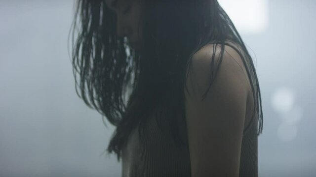 Beautiful contemporary dancer slowly begins to rock back and forth, leans back and begins to dance in misty industrial warehouse