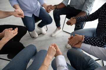 Close up diverse people sitting on chairs in circle at group training counselling session, holding hands, psychological help and treatment concept, drug or alcohol addiction rehabilitation - obrazy, fototapety, plakaty