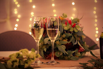 Champagne flutes on bridal table at wedding reception decorated with letters E and J with bokeh...