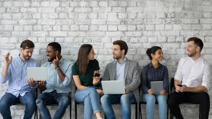 Friendly diverse candidates talking, chatting and using gadgets while waiting for job interview,...