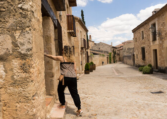 Fototapeta na wymiar Blonde girl knocking on a village door with facades and cobbled floor
