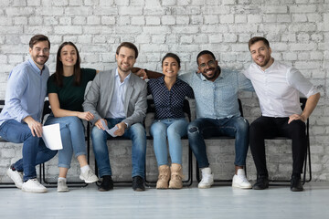 Portrait smiling diverse candidates business people hugging, siting in row in queue, successful...
