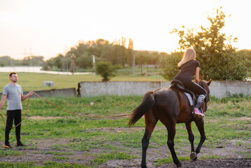 A young and pretty girl is learning to ride a thoroughbred Mare on a summer day at the ranch. Horse...