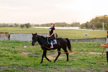 A young and pretty girl is learning to ride a thoroughbred Mare on a summer day at the ranch. Horse...