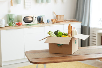 Background image of cardboard box with food on wooden table in minimal kitchen interior, copy space