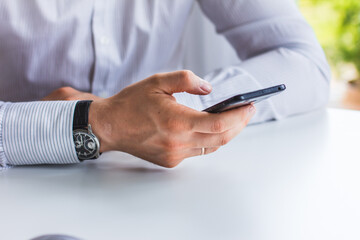 Image of hands of a man who is sitting at a table holding a phone