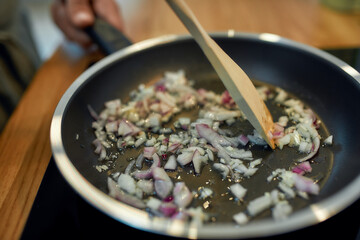 Close up of sauteed onion and garlic in the frying pan. Man preparing dinner. Cooking at home concept