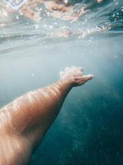 Obraz na płótnie Canvas Vertical photo of white man's arm under crystal clear sea water with algae under it