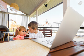 Obraz premium Small smiling kids brother and sister laugh and play laptop, communicate video conference chatting. Spacious cozy home interior.