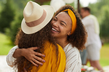 Portrait of young African-American woman hugging friend and smiling cheerfully while enjoying...