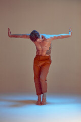 Young man dancing expressive dance without shirt in neon light in studio. Dance school poster. Body with tattoos