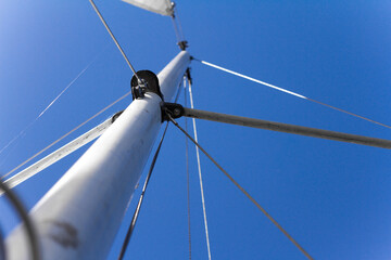 Bottom view of mast and sail of yacht on blue sky background, selective focus