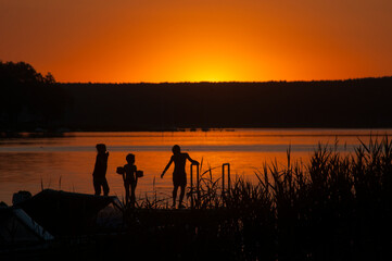 Dzieci kąpią się w jeziorze podczas widowiskowego zachodu słońca - obrazy, fototapety, plakaty