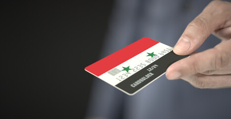 Man gives plastic bank card with printed flag of Syria. Fictional numbers