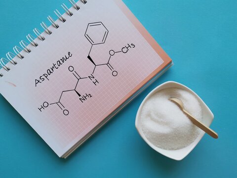 Structural chemical formula of aspartame molecule with artificial sweetener in white bowl. Aspartame is an artificial sweetener used as a sugar substitute in low-calorie food and drinks.