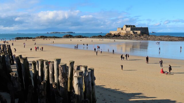 Saint-Malo en Bretagne, vue panoramique sur la mer et la grande plage du Sillon, avec des promeneurs, le Fort National et des brise-lames (France)