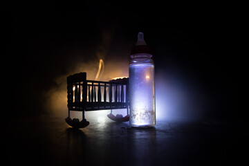 Close up of baby bottle at wooden table on dark toned foggy background with light. Creative artwork...