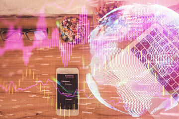 Double exposure of financial graph hologram over desktop with phone. Top view. Mobile trade platform concept.