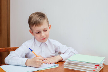 the boy is sitting at the table, holding a pen, next to notebooks and textbooks