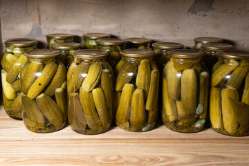 pickles or salted cucumbers in glasses on a wooden shelf in cellar