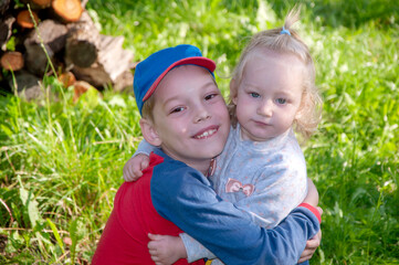 Young boy hugging his smaller adorable sister during their summer walking in the garden, brothers love, family relationship, emotional close-up portrait, outdoor lifestyle.