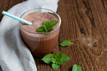 Chocolate cocktail, drink, smoothie in a glass glass with a mint sprig and a reusable straw on a linen napkin on a wooden background. Dessert drinks. Place for text