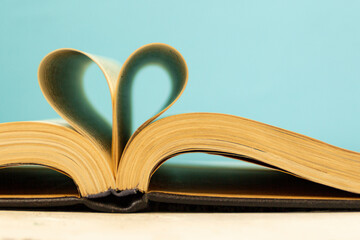 The pages of the book are curved in the shape of a heart. Opened book on a blue background. Back to school theme concept. Bibliophile