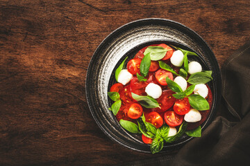 Caprese salad with ripe red tomatoes and mozzarella cheese with fresh green basil leaves. Italian food. Top view, wooden background