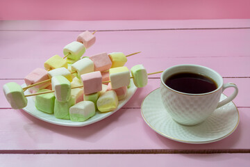 Cup of aromatic coffee americano and plate with marshmallows on pink wooden table. Cozy breakfast...