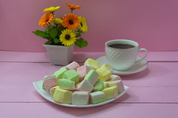 Marshmallows from different fruits on white dish close-up. A cup of strong coffee on pink wooden...