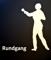 Schwarzes Hinweisschild mit Abbildung einer Person: Rundgang © thauwald-pictures