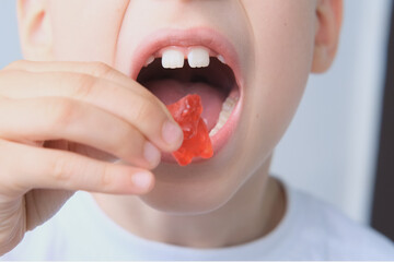 boy, kid holds in his mouth and eats gelatinous sweets, gummy bear, concept of children's delicacy, healthy and unhealthy food, halal food