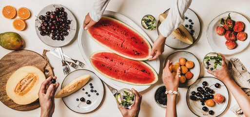 Summer tropical fruit party table. Flat-lay of people having lunch with various fruits, berries, watermelon and lemonade over white background, top view. Clean eating, vegan, fruiterian food concept