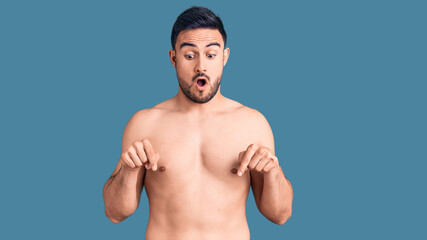 Young handsome man wearing swimwear pointing down with fingers showing advertisement, surprised face and open mouth