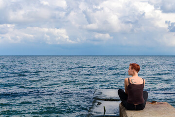 Woman Sitting On Pier Over Sea Against Sky, turns his head towards the wind, the concept of freedom, relaxation and rest
