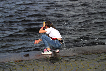 a little girl in blue jeans and a white blouse is playing with water