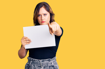 Fototapeta na wymiar Young beautiful caucasian woman holding blank empty paper pointing with finger to the camera and to you, confident gesture looking serious