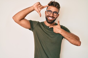 Young hispanic man wearing casual clothes and glasses smiling making frame with hands and fingers...