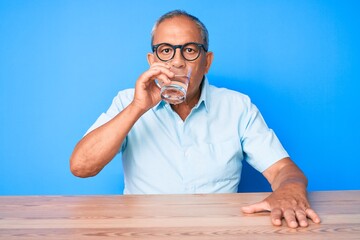 Handsome senior man sitting on the table at home drinking a glass of fresh water