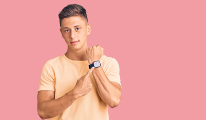 Young handsome man wearing casual clothes in hurry pointing to watch time, impatience, looking at...