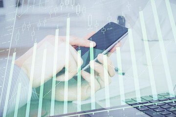 Double exposure of man's hands holding and using a digital device and forex graph drawing. Financial market concept.
