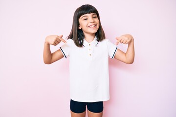 Young little girl with bang wearing sportswear looking confident with smile on face, pointing...